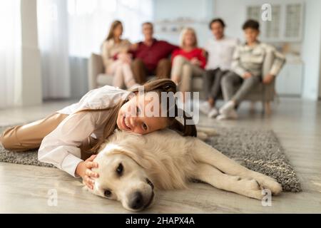 Entzückendes kleines Mädchen, das mit einem goldenen Retriever-Hund auf dem Boden liegt und zu Hause mit einem Haustier umarmt und kuschelt. Familienzeiten Stockfoto