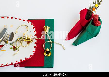 Stilvoller, leerer Weihnachtsteller und Besteck auf weißer Oberfläche mit grünen und roten Servietten, gefaltet ein kleiner Elfschuh Stockfoto