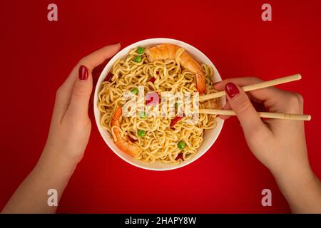 Weibliche Hände mit Schale Garnelennudeln auf rotem Hintergrund Stockfoto