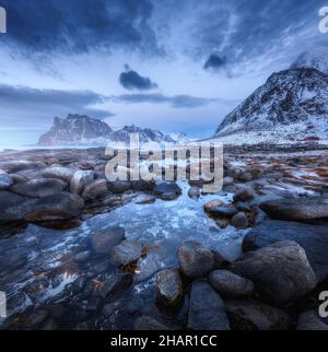 Küste mit Steinen und verschwommenem Wasser, gegen verschneite Berge Stockfoto