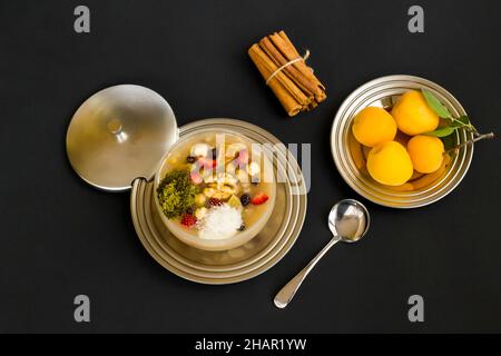 Traditionelles türkisches Dessert Asure oder Noah's Ark Pudding auf schwarzer Oberfläche mit Aprikose und Zimtstangen Stockfoto