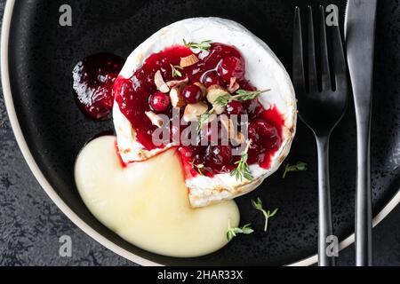 Gebackener Camembert-Käse mit Preiselbeeren und Nüssen auf schwarzem Teller serviert, Draufsicht Stockfoto