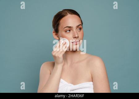 Ingwer Frau trägt Handtuch Reinigung ihr Gesicht mit Wattepad isoliert auf blauem Hintergrund Stockfoto
