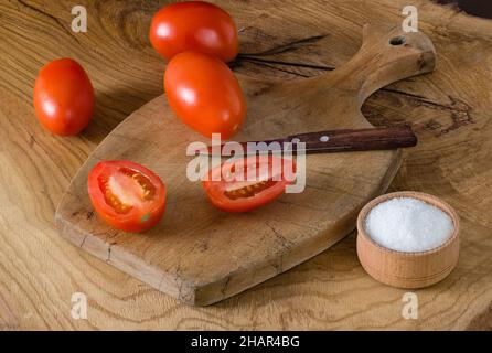 Viele ganze Tomaten in Form von Pflaumen und einem Schnitt liegen auf einem hölzernen Schneidebrett Stockfoto