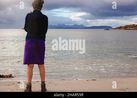 Ein Besucher, der von einem der weißen Sandstrände von Ardtoe auf der Halbinsel Ardnamurchan, Westschottland, die Aussicht auf die kleinen Inseln genießt Stockfoto