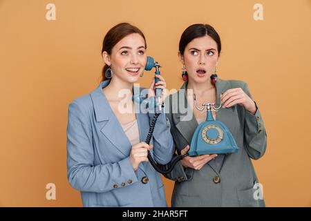 Junge zwei Frauen in Jacke posiert mit Retro-Telefon isoliert auf gelbem Hintergrund Stockfoto