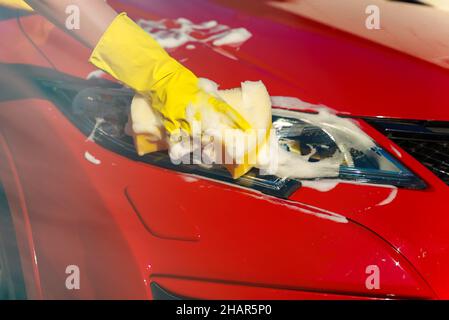 Frau in Handschuhen wäscht Autoscheinwerfer mit Schwamm. Stockfoto