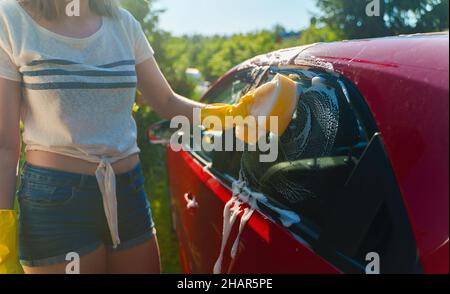 Frau in Handschuhen wäscht Autofenster mit Schwamm. Stockfoto