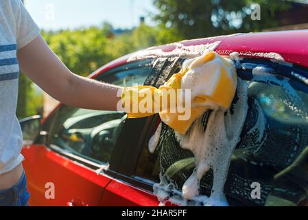 Frau in Handschuhen wäscht Autofenster mit Schwamm. Stockfoto