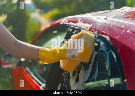 Frau in Handschuhen wäscht Autofenster mit Schwamm. Stockfoto