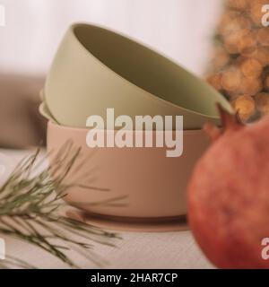 Set aus Silikon-Babyschalen. Zwei aufeinander gestapelte Schalen mit Granatapfel vor dem Hintergrund des Weihnachtsbaums. Kreative Unschärfe und Maserung. Quadratisches Fr. Stockfoto