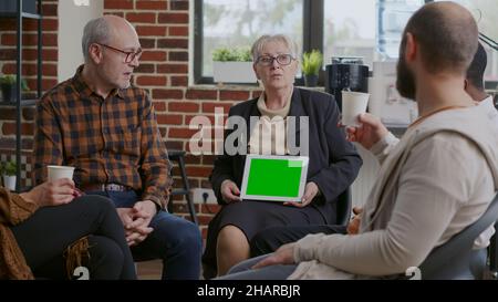 Therapeut hält Tablet mit horizontalem grünen Bildschirm bei einem Treffen mit Menschen. Psychiaterin zeigt Chroma-Schlüssel und isolierte Modell-Vorlage auf dem Display für Patienten mit sucht. Stockfoto