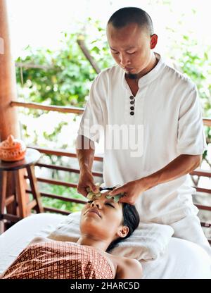 Frau, die in Kamalaya, Koh Samui, Thailand, eine Guasha-Gesichtsbehandlung erhält. Eine Frau erhält eine Guasha-Gesichtsbehandlung, eine traditionelle chinesische Heilpraxis mit Jade. Stockfoto
