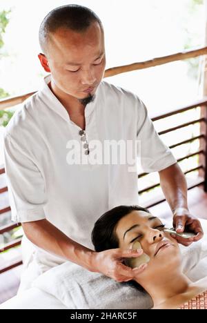 Frau, die in Kamalaya, Koh Samui, Thailand, eine Guasha-Gesichtsbehandlung erhält. Eine Frau erhält eine Guasha-Gesichtsbehandlung, eine traditionelle chinesische Heilpraxis mit Jade. Stockfoto