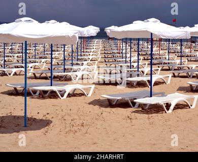 Viele Sonnenschirme und Liegen mit Blick auf eine Horizont-Linie über das Meer am leeren Strand Stockfoto