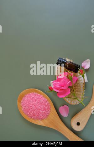 Ätherisches Rosenöl und Kosmetiksalz mit Rosenextrakt.Aromatherapie . Glasflaschen, Rosenblumen und Kosmetiksalz auf grünem Hintergrund. Stockfoto