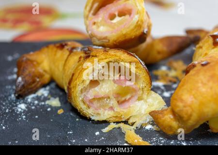 Frisch gebackene Croissants gefüllt mit Schinken und geschmolzenem Käse auf einem grauen Schieferteller Stockfoto