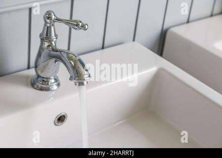 Wasser läuft aus einem offenen Wasserhahn mit weißem Waschbecken Hintergrund Stockfoto