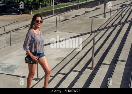 Eine Aufnahme in voller Länge von einer schönen Latina-Frau, die lächelt und an einem sonnigen Tag eine Betontreppe klettert. Stockfoto