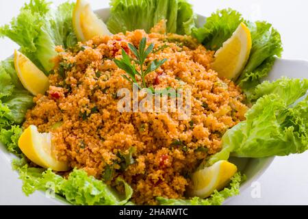 Traditioneller türkischer Weizen, Kisir Bulgur Salat mit Salat und Zitronenscheiben auf weißem Teller, Nahaufnahme Stockfoto