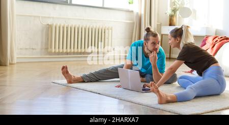 Junges Paar, das sich zu Hause vor einem Laptop-Monitor streckt. Konzept eines gesunden Lebensstils und sich selbst in Form zu halten. Foto 2x1 formatieren. Stockfoto
