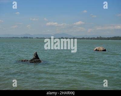 Felsiges Riff und Stein im grünen Wasser des Meeres mit Berg und blauem Himmel im Hintergrund, Thailand Stockfoto