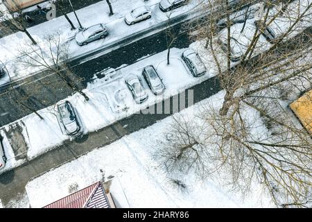 Schneebedeckte Bäume und Autos auf dem Parkplatz. Wintersaison in der Stadt. Luftaufnahme von oben von fliegender Drohne. Stockfoto