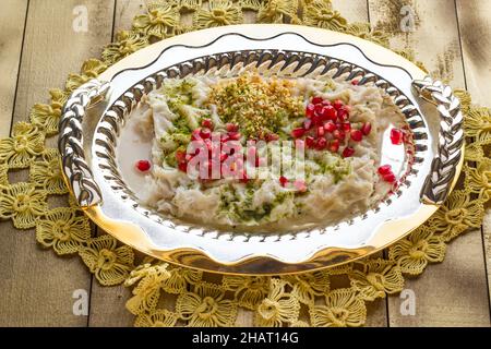 Traditionelles türkisches Ramadan Dessert, Gulac in elegantem glänzendem Tablett auf Holzoberfläche mit handgefertigtem Spitzentuch Stockfoto