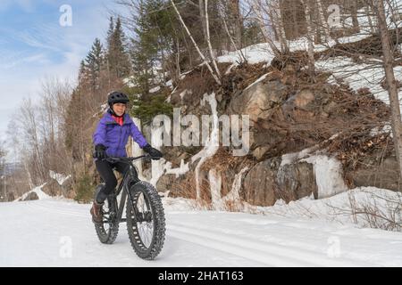 Fatbike im Winter. Frau Fat Biker Reiten Fett Fahrrad im Schnee in Winterwald Berglandschaft. Frau lebt gesund im Freien aktiv Stockfoto