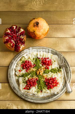 Köstliches, milchiges Ramadan Dessert, Gulac Vintage Teller auf dem Holztisch mit Granatapfelfrüchten. Stockfoto