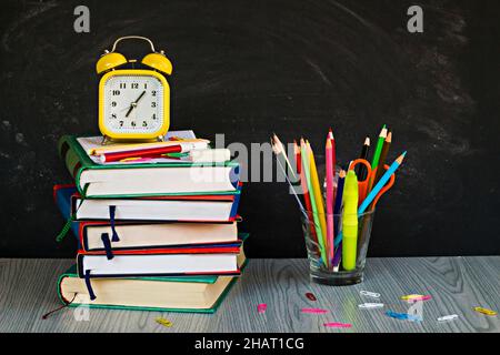 Ein gelber Vintage-Wecker und bunte Schulbedarf vor Kreide staubige Kreidetafel.konzeptuelles Bild von Bildung Stockfoto