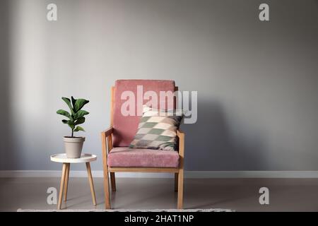 Moderner Sessel und Tisch mit Zimmerpflanzen in der Nähe einer hellen Wand Stockfoto