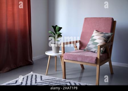 Gemütlicher Holzsessel mit Zimmerpflanzen auf dem Tisch in der Nähe der hellen Wand Stockfoto