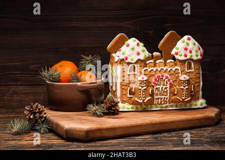 Brett mit Lebkuchenhaus und Mandarinen auf Holzhintergrund Stockfoto