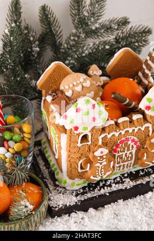 Board mit schönen Lebkuchenhaus, Mandarinen, Schnee und Leckereien auf dem Tisch Stockfoto