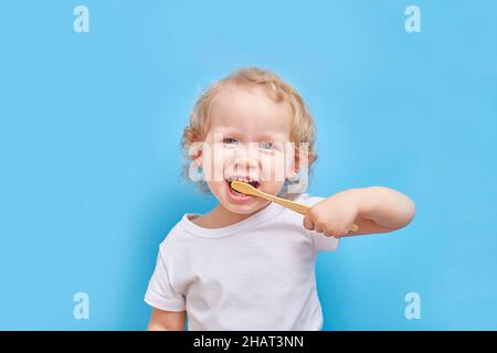 Das linkshändige Kind putzt seine Zähne mit einer Bambuszahnbürste auf einem einfachen Hintergrund mit einem Platz für Text. Stockfoto