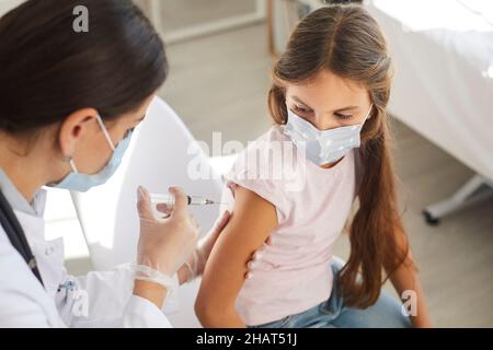 Krankenschwester oder Arzt in der Klinik, die einem kleinen Kind eine Grippe- oder Covid 19-Impfstoffinjektion verabreichten Stockfoto