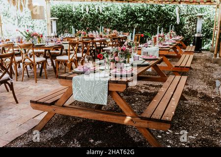 Terrasse mit Tischen mit Blumen und Tellern auf dem Tisch, die für Hochzeitsempfänge in Lateinamerika dekoriert sind Stockfoto