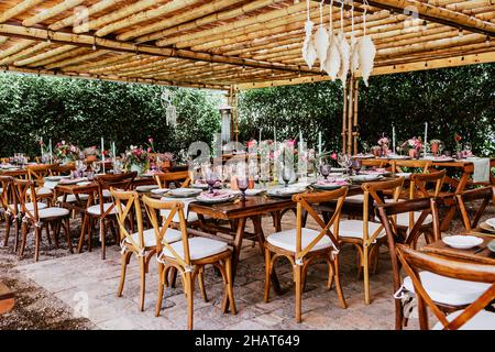 Terrasse mit Tischen mit Blumen und Tellern auf dem Tisch, die für Hochzeitsempfänge in Lateinamerika dekoriert sind Stockfoto