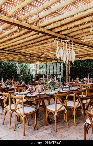 Terrasse mit Tischen mit Blumen und Tellern auf dem Tisch, die für Hochzeitsempfänge in Lateinamerika dekoriert sind Stockfoto