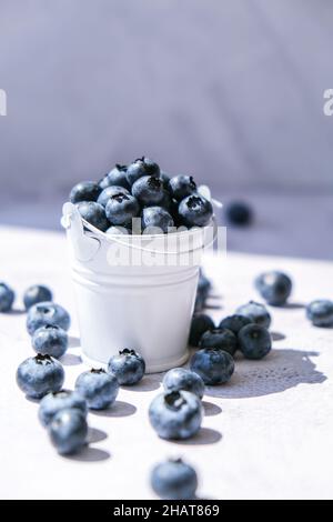 Heidelbeeren in einem kleinen Eimer auf Betongrund. Gesunde Bio saisonalen Obst Hintergrund. Bio-Lebensmittel. Gesunder Sommersnack. Speicherplatz kopieren Stockfoto