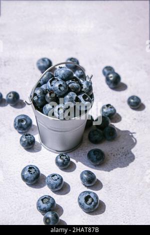 Heidelbeeren in einem kleinen Eimer auf Betongrund. Gesunde Bio saisonalen Obst Hintergrund. Bio-Lebensmittel. Gesunder Sommersnack. Speicherplatz kopieren Stockfoto