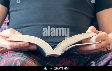 Mann, der zu Hause ein Buch liest und umdreht. Nahaufnahme einer Person Hände mit einem geöffneten weißen Buch. Stockfoto