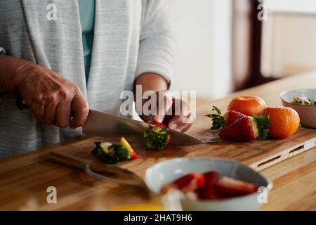 Hände von älteren Frauen, die in der modernen Küche Erdbeeren hacken. Vorbereitung einer gesunden Mahlzeit zum Frühstück. Stockfoto