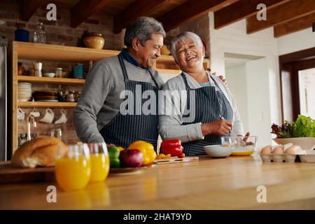 Biracial älteren Pärchen lachen glücklich Kochen in der Küche. Der Arm des Mannes um die Frau, ein gesunder Lebensstil im Ruhestand. Stockfoto