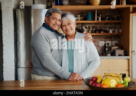 Porträt eines glücklich pensionierten älteren Birazialpaares, das sich gegenseitig hält. Gesunder Lebensstil, stehend in der modernen Küche. Stockfoto