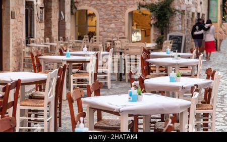 Griechische Taverne Open Air leere Sitze, Steinmauer Hintergrund, Areopoli, Mani Griechenland. Typisches Restaurant mit Holztischen und Stühlen auf Kopfsteinpflaster Stockfoto