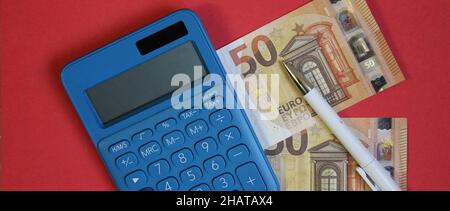 Draufsicht auf einen blauen Rechner, Stift und Euro-Banknote auf blauem Hintergrund Stockfoto