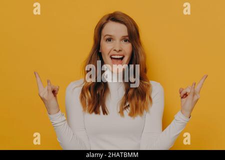 Sorgloses Teenager-Mädchen mit braunen welligen Haaren und durchbohrter Zunge, die Rock and Roll-Geste oder Zeichen von Hörnern zeigt Stockfoto