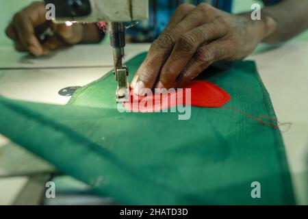 Ein Arbeiter näht die Nationalflagge von Bangladesch vor dem Siegesstag in Narayanganj, am Stadtrand von Dhaka, Bangladesch, am 14. Dezember 2021. Am 16. Dezember wurde zum Gedenken an den Sieg der Streitkräfte Bangladeschs über die pakistanischen Streitkräfte im Befreiungskrieg von Bangladesch im Jahr 1971 ein Siegestag gefeiert. Der Kommandeur der pakistanischen Streitkräfte, General AAK Niazi, gab sich mit seinen Truppen den alliierten Kräften von Bangladesch hin, was das Ende des 9 Monate andauernden Bangladesh Liberation war und 1971 den Völkermord in Bangladesch und die offizielle Abspaltung Ostpakistans nach Bangladesch bedeutete. Foto von S Stockfoto